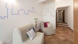 A modern living room with two sofas, a white wall with a cityscape mural, and a wooden staircase leading to a bathroom. - Faenza Double (Florence)