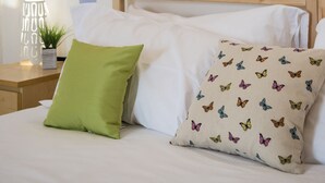 A bedroom with a bed, a green pillow, a pillow with butterfly prints, a wall with a tree decal, and a bedside table with a lamp and a plant. - Faenza Double (Florence)