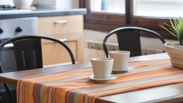 A dining area with a table set for two, chairs, a striped tablecloth, and a window with a view of buildings. - Faenza Double (Florence)