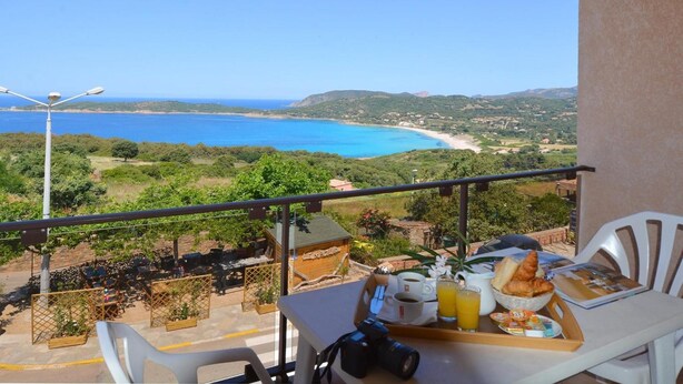 A balcony with a table set for breakfast, overlooking a coastal landscape with a beach and hills. - Hotel le Saint Jean (Cargese)