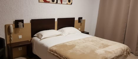 Habitación de hotel con una cama, cabecero, mesita de noche, teléfono y una obra de arte en la pared.
