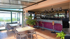 A restaurant with outdoor seating, a bar area, and a view of the landscape. - Hotel le Saint Jean (Cargese)