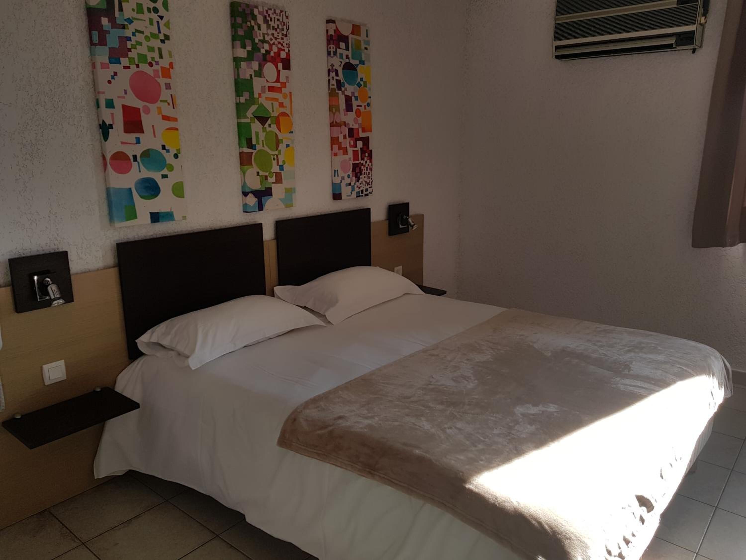 Une chambre à coucher comprenant un lit, deux tables de chevet et trois œuvres d’art abstraites accrochées au mur.