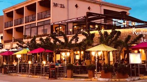 A hotel with a bar and restaurant on the ground floor, outdoor seating with umbrellas, and a stone facade. - Hotel le Saint Jean (Cargese)