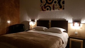 A hotel room with a large bed, two bedside tables, a chair, and a wall-mounted artwork. - Hotel le Saint Jean (Cargese)