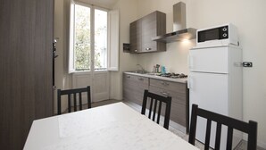 A compact kitchen with a white refrigerator, a stove, and a microwave. There is a window with a view of trees outside. - Fortezza Second floor (Florence)