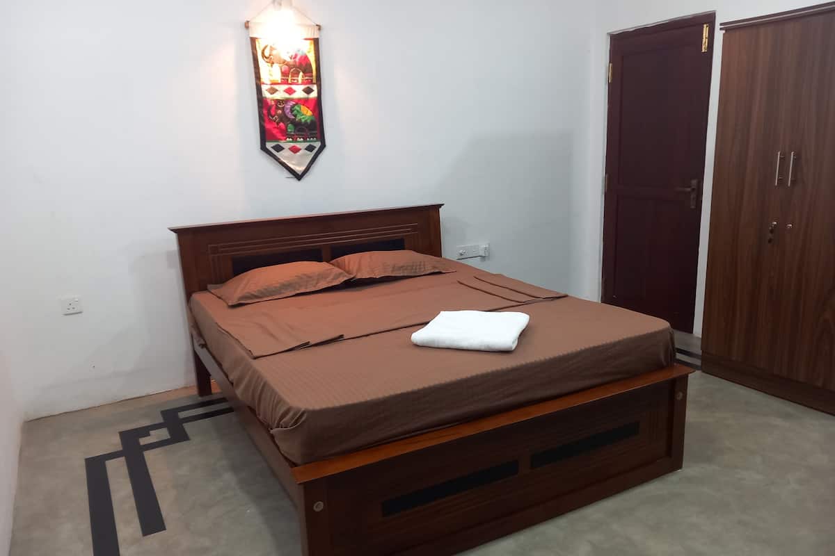 Una cama individual con estructura de madera y ropa de cama marrón, una lámpara fijada a la pared y un armario.
