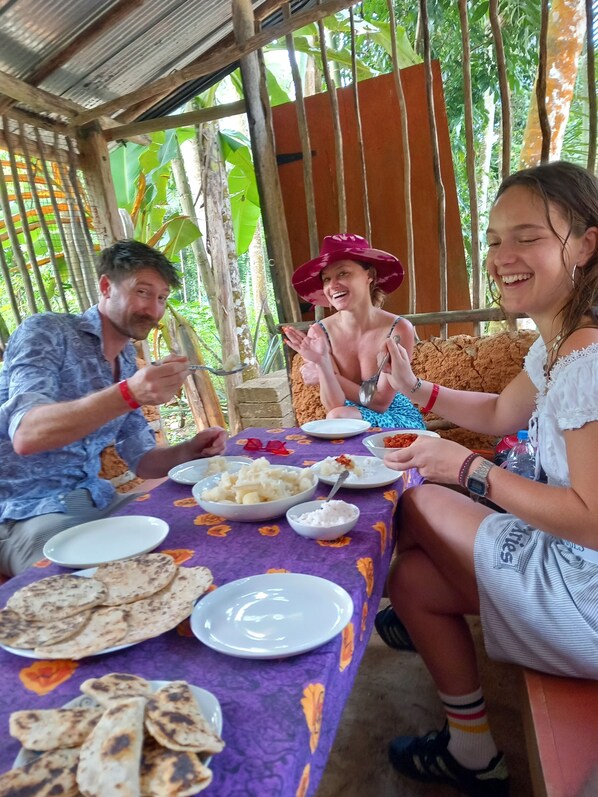 A group of people dining at an outdoor table with a purple tablecloth, surrounded by greenery.