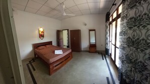A bedroom with a bed, a ceiling fan, a wall-mounted light, a wardrobe, and a window with patterned curtains.