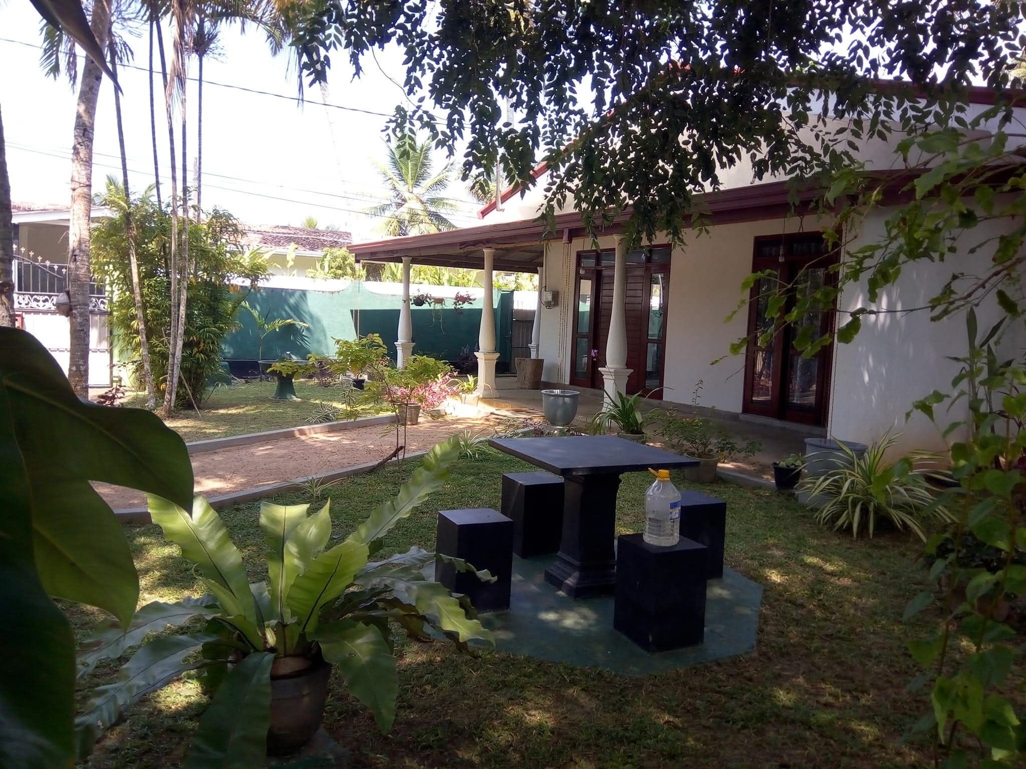A courtyard with a table and chairs, surrounded by potted plants and a building with a covered entrance.