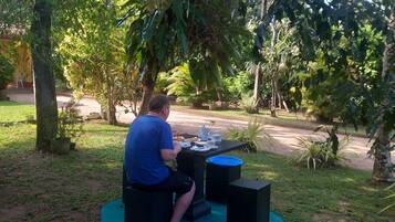 A person sitting at an outdoor table with a green mat, surrounded by trees and plants.