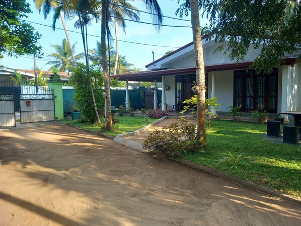 A residential property with a paved driveway, a covered porch, and a well-maintained lawn. - Shenya Villa (Bentota)