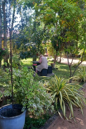 A garden with a person sitting at a table, surrounded by various plants and trees. - Shenya Villa (Bentota)