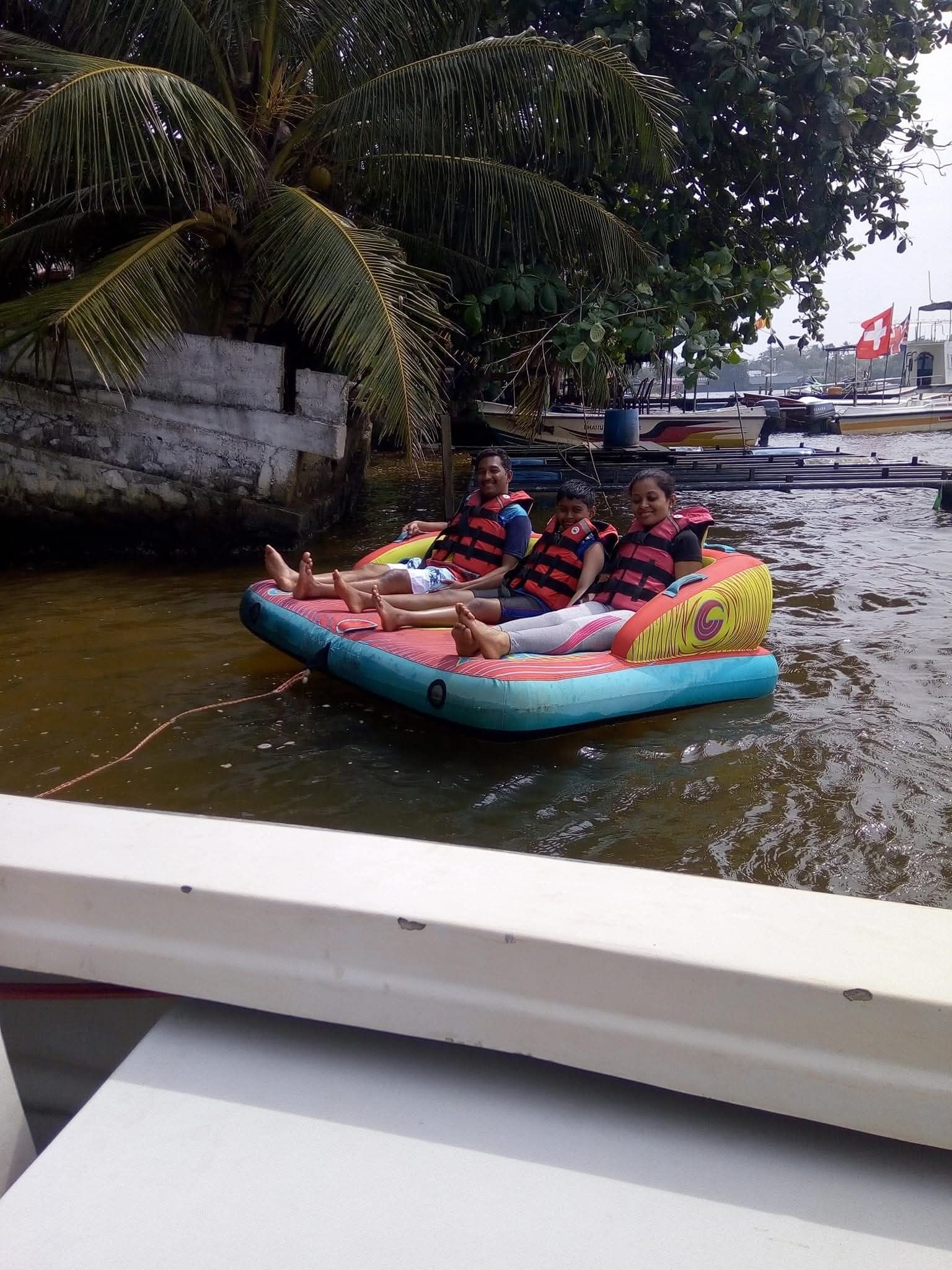 A group of people on a colorful inflatable raft in a body of water, with boats and a Swiss flag in the background.