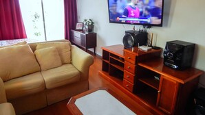 A living room with a sofa, a TV mounted on the wall, a wooden cabinet, and a small table. - Residencial Encantos de Gramado (Gramado)