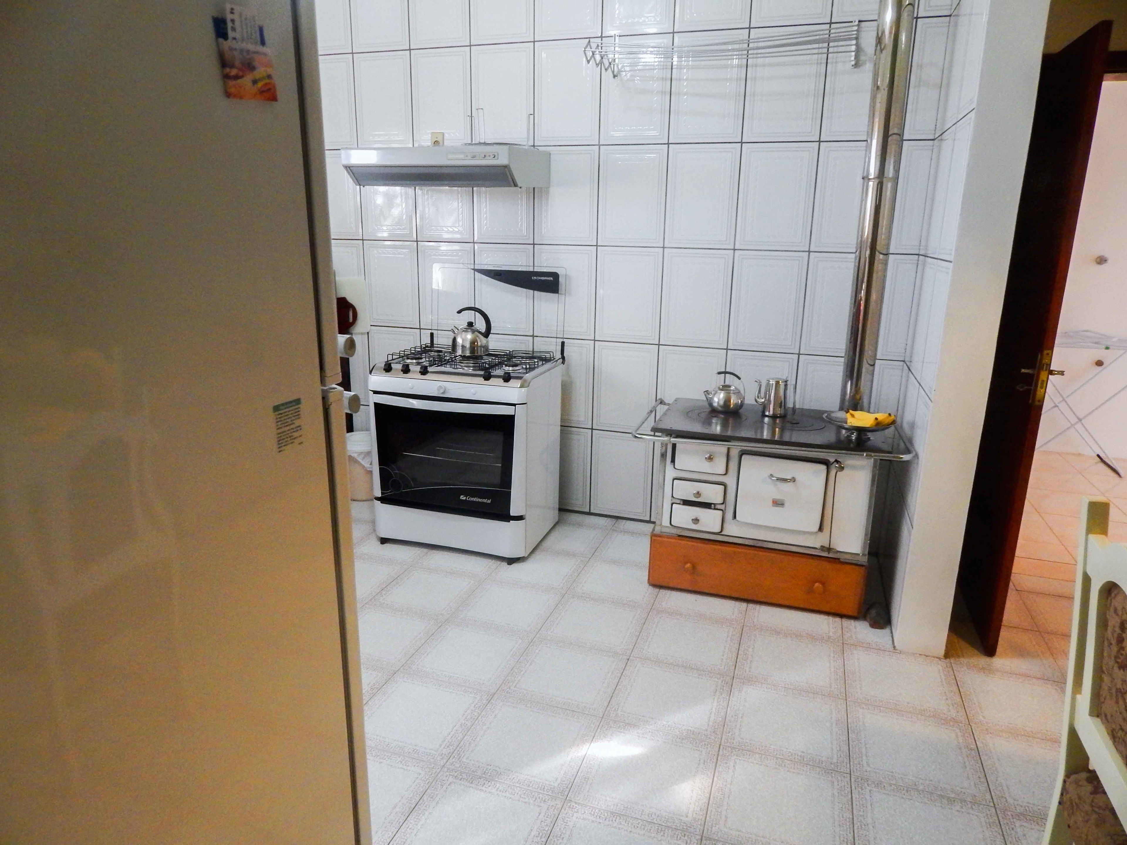A compact kitchen with white tiled walls, a gas stove, a built-in oven, and a small countertop with a kettle and a cup.