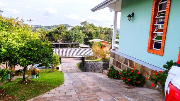 A pathway leading to a house with a tiled roof, a stone wall, and a car parked nearby. - Residencial Encantos de Gramado (Gramado)