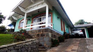 A two-story house with a stone foundation, a balcony with white railings, and a car parked in the driveway. - Residencial Encantos de Gramado (Gramado)