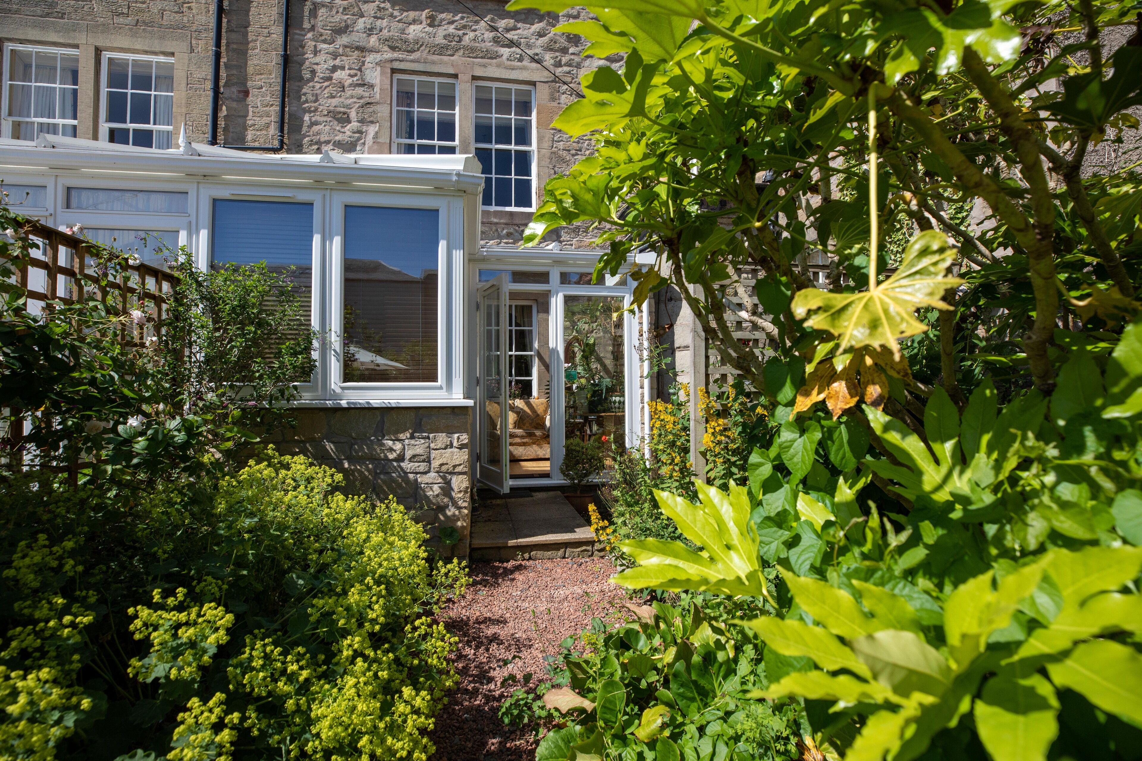 A traditional stone building with a conservatory and a garden.