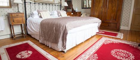 Un dormitorio con una cama grande, suelo de madera y alfombras con motivos rojos y blancos.