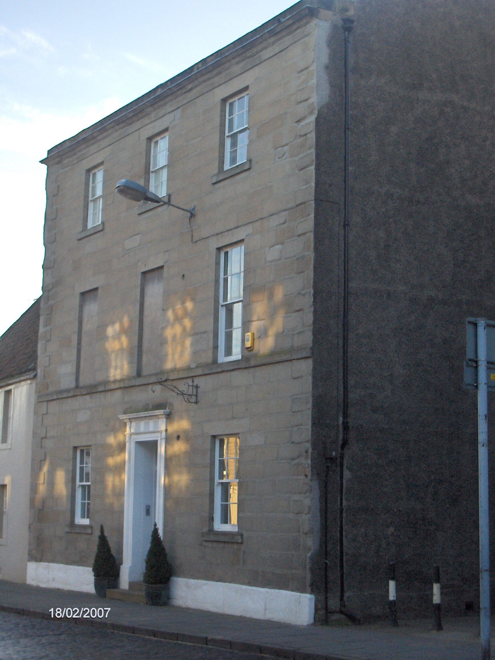 Un edificio a due piani con una porta bianca e diverse finestre. Davanti alla porta ci sono due piccoli vasi con piante.