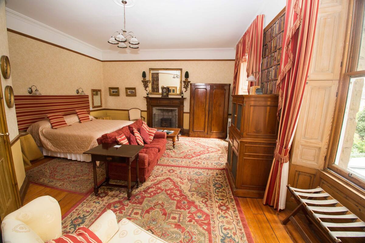 Un dormitorio tradicional con una cama grande, una chimenea, un armario de madera y una ventana con cortinas.