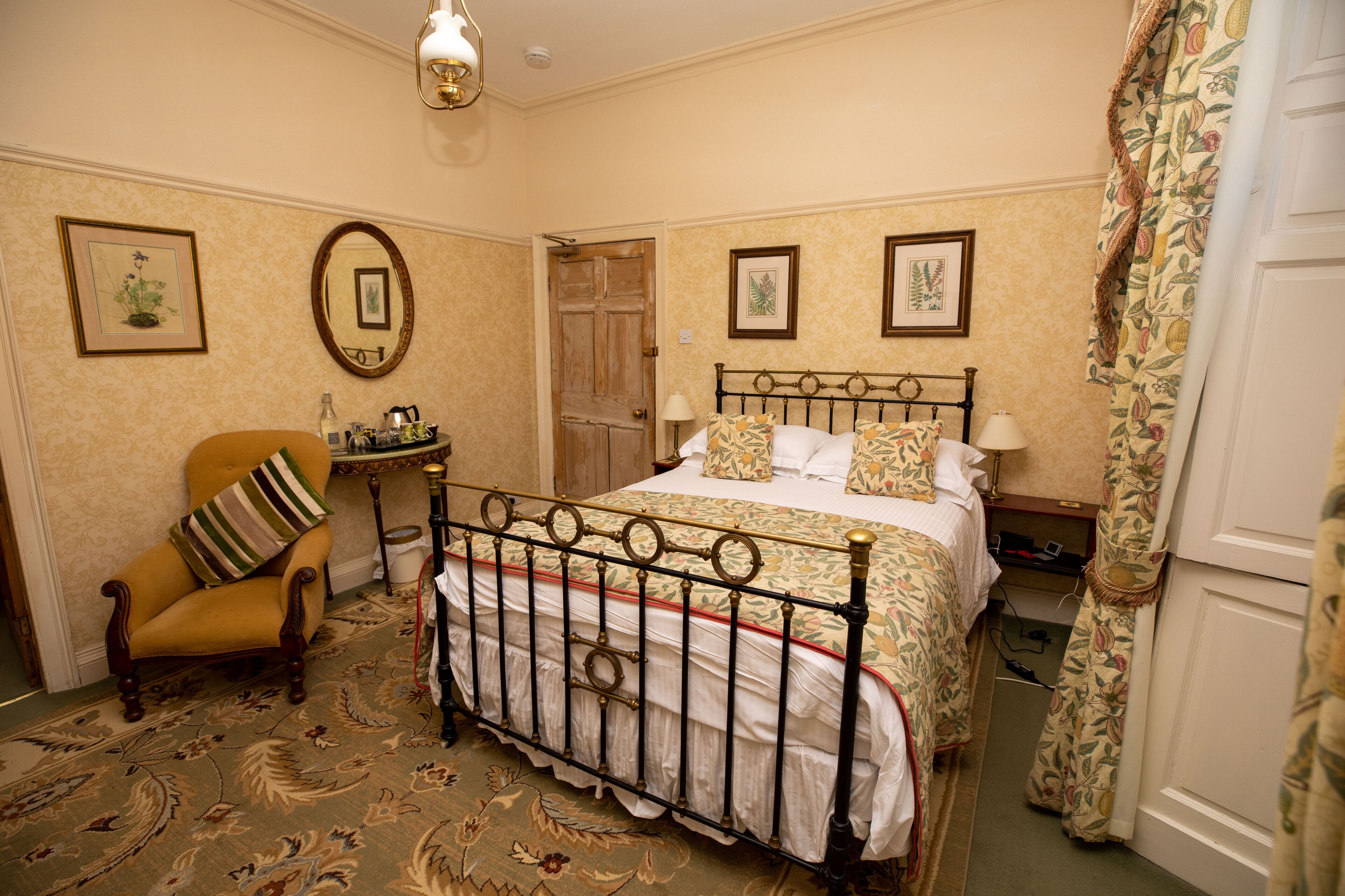 A traditional bedroom with a four-poster bed, a wooden chair, and a small table with a lamp.