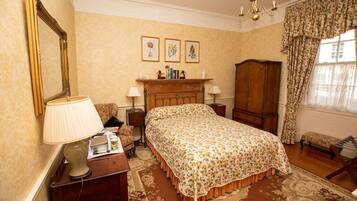 A bedroom with a bed, a nightstand, a lamp, a chair, a wardrobe, and a mirror. There are three framed pictures on the wall above the bed.