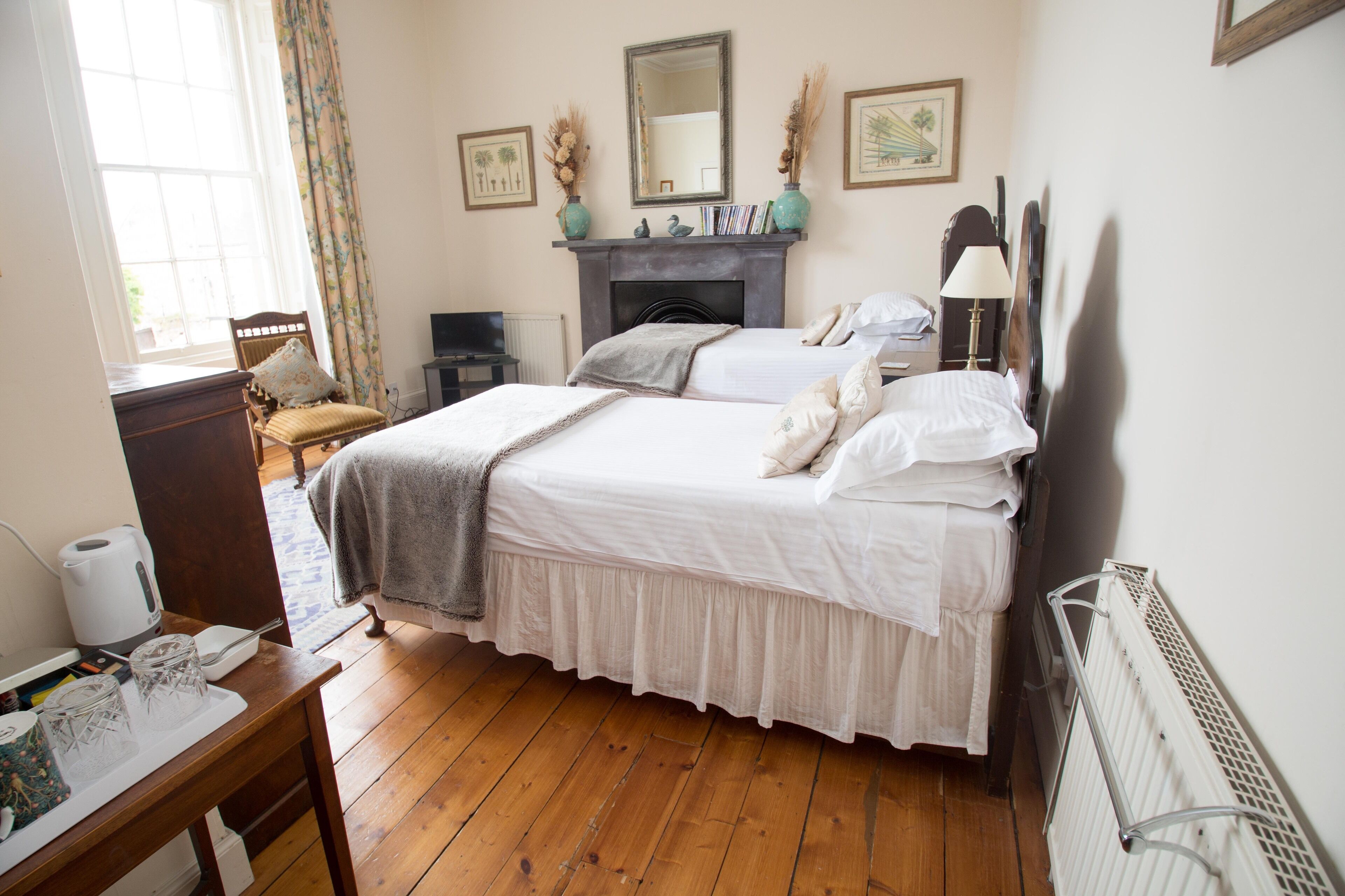 A bedroom with two beds, a fireplace, a mirror, and a radiator.