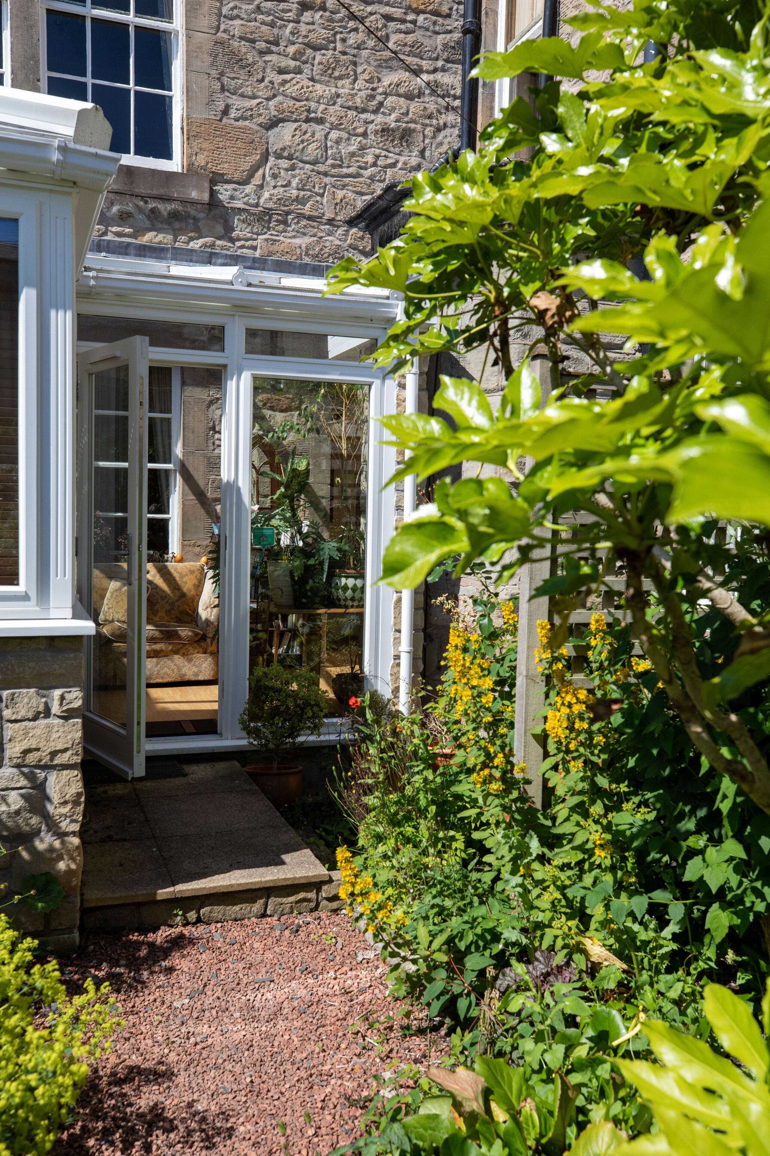 A stone building with a covered porch, a garden with various plants, and a bench.