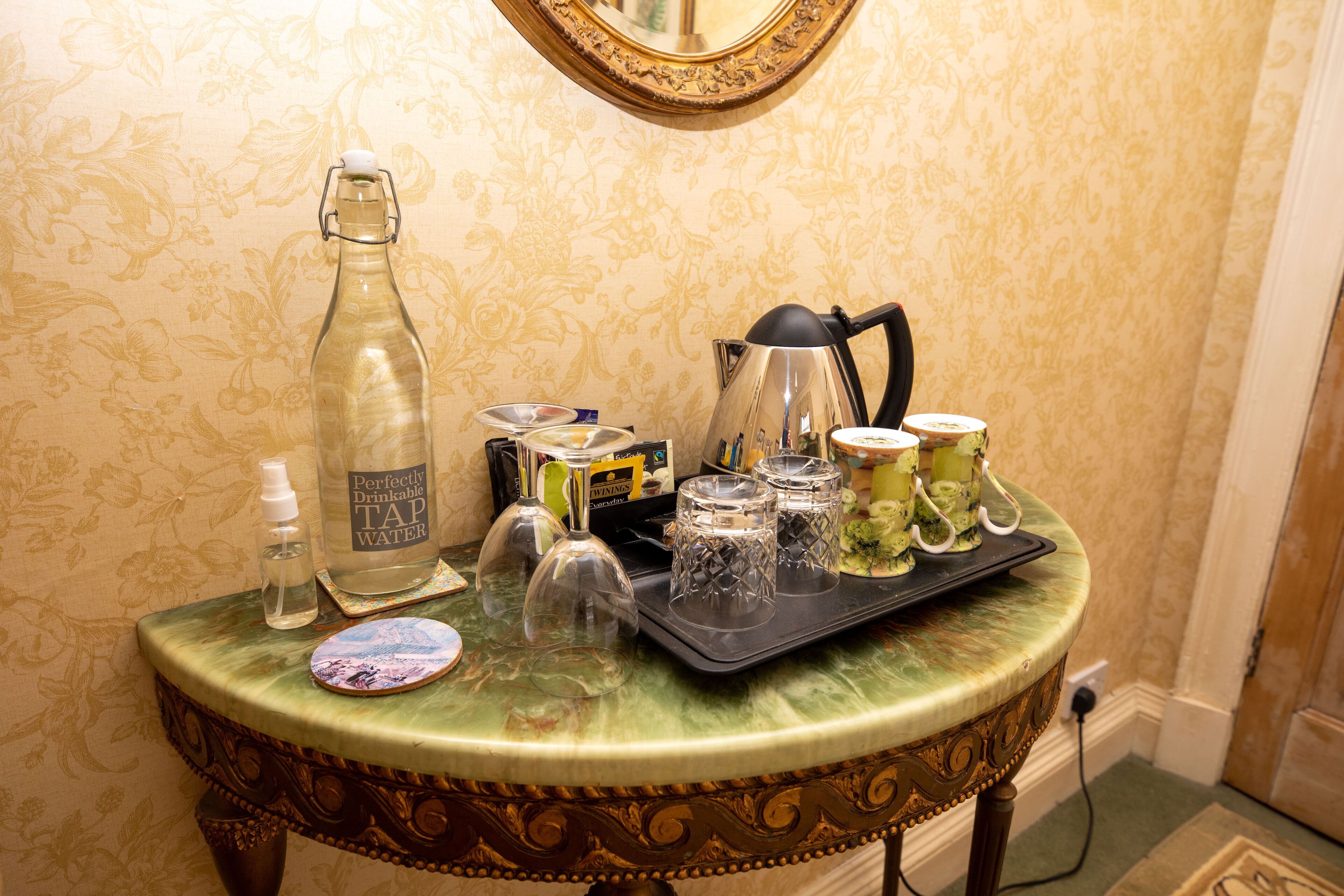 A table with a bottle of water, a glass, a tray with glasses, and a kettle.