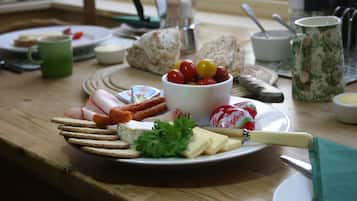 Un desayuno con un plato de queso, galletas y tomates, una taza verde y una cafetera sobre una mesa de madera.
