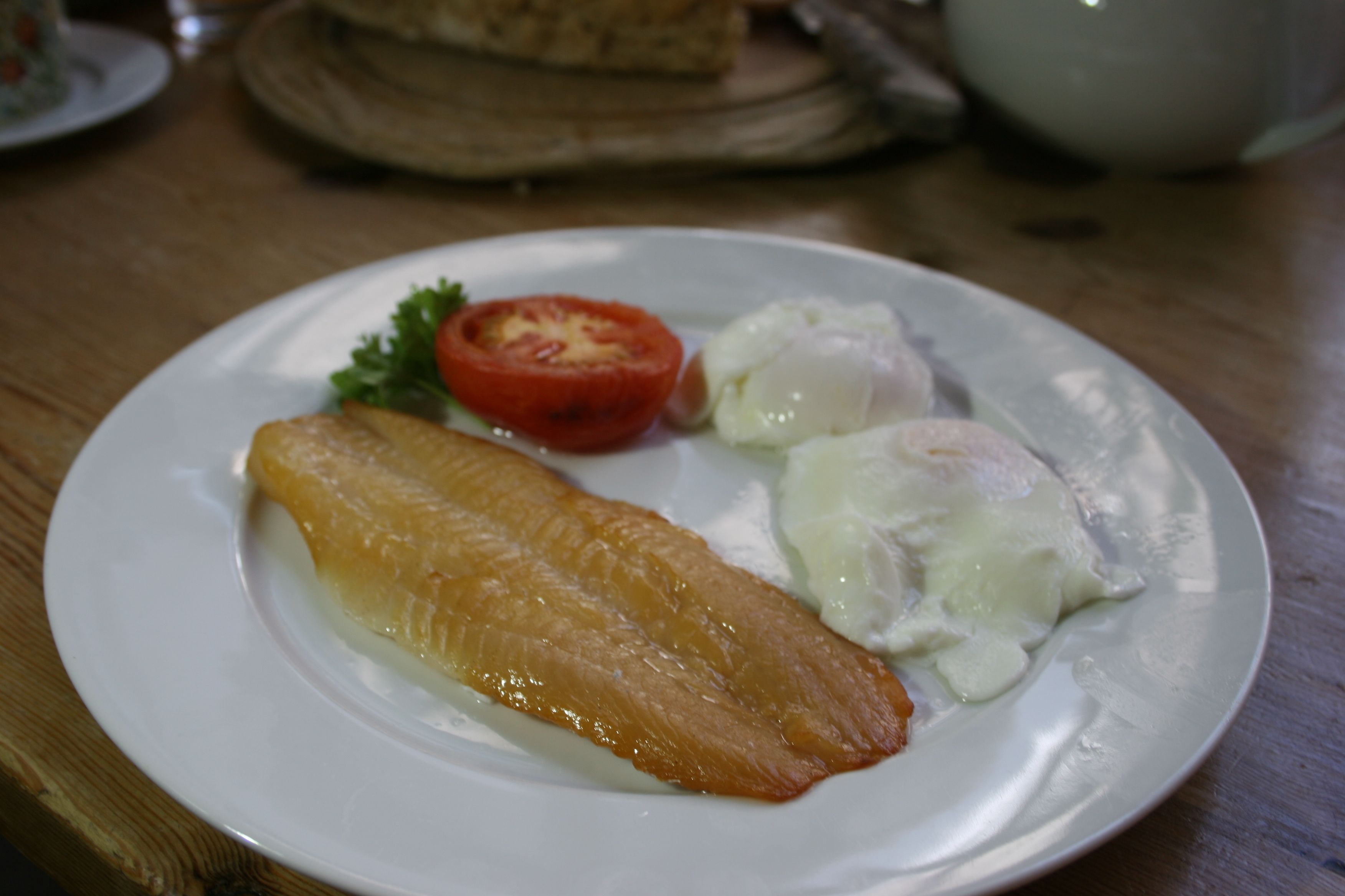 Un plato con un trozo de pescado, una rodaja de tomate y una cucharada de salsa sobre una mesa de madera.