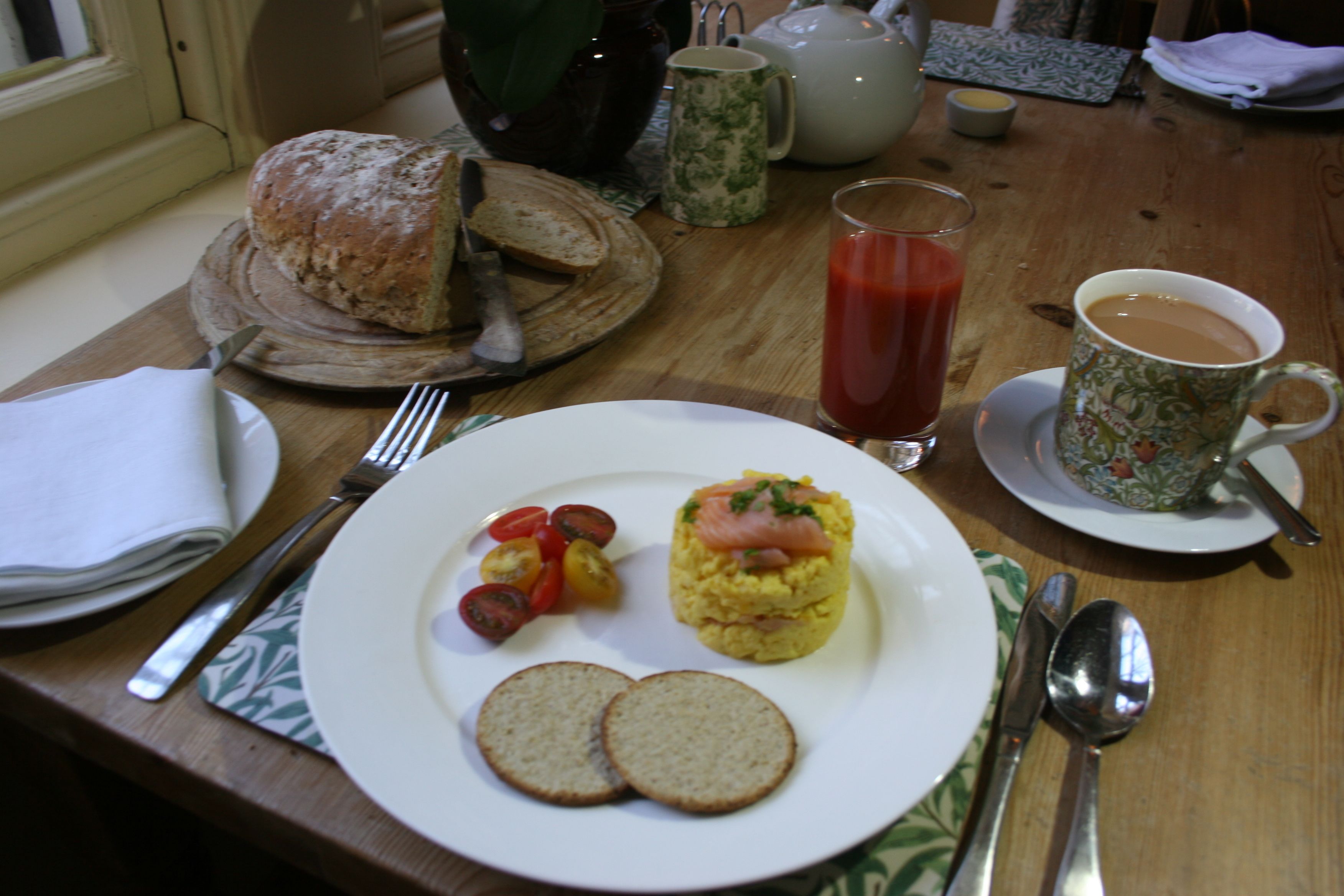 Desayuno con un plato de huevos, tomates y pan, un vaso de jugo y una taza de café sobre una mesa de madera.