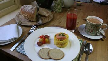 Desayuno con un plato de huevos, tomates y pan, un vaso de jugo y una taza de café sobre una mesa de madera.