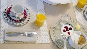 Een ontbijtsetting met een kop, schoteltje, lepel, glas sinaasappelsap en een bord met yoghurt, bessen en een klein bakje granola.