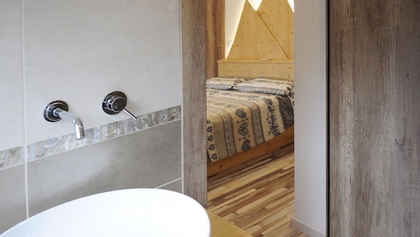 Een badkamer met een wit wastafel, twee chromen kranen en een houten vloer.