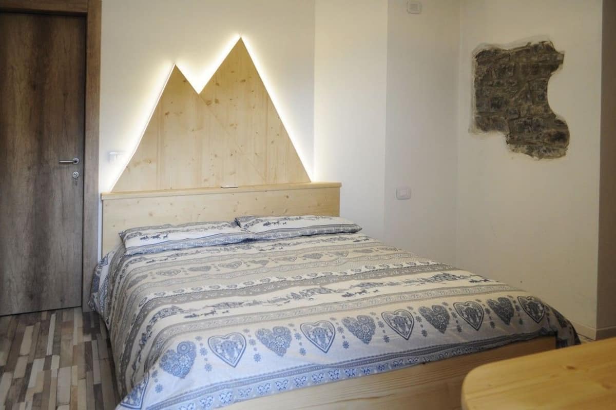 Une chambre à coucher avec une tête de lit en bois, une literie à motifs et un décor mural en pierre.
