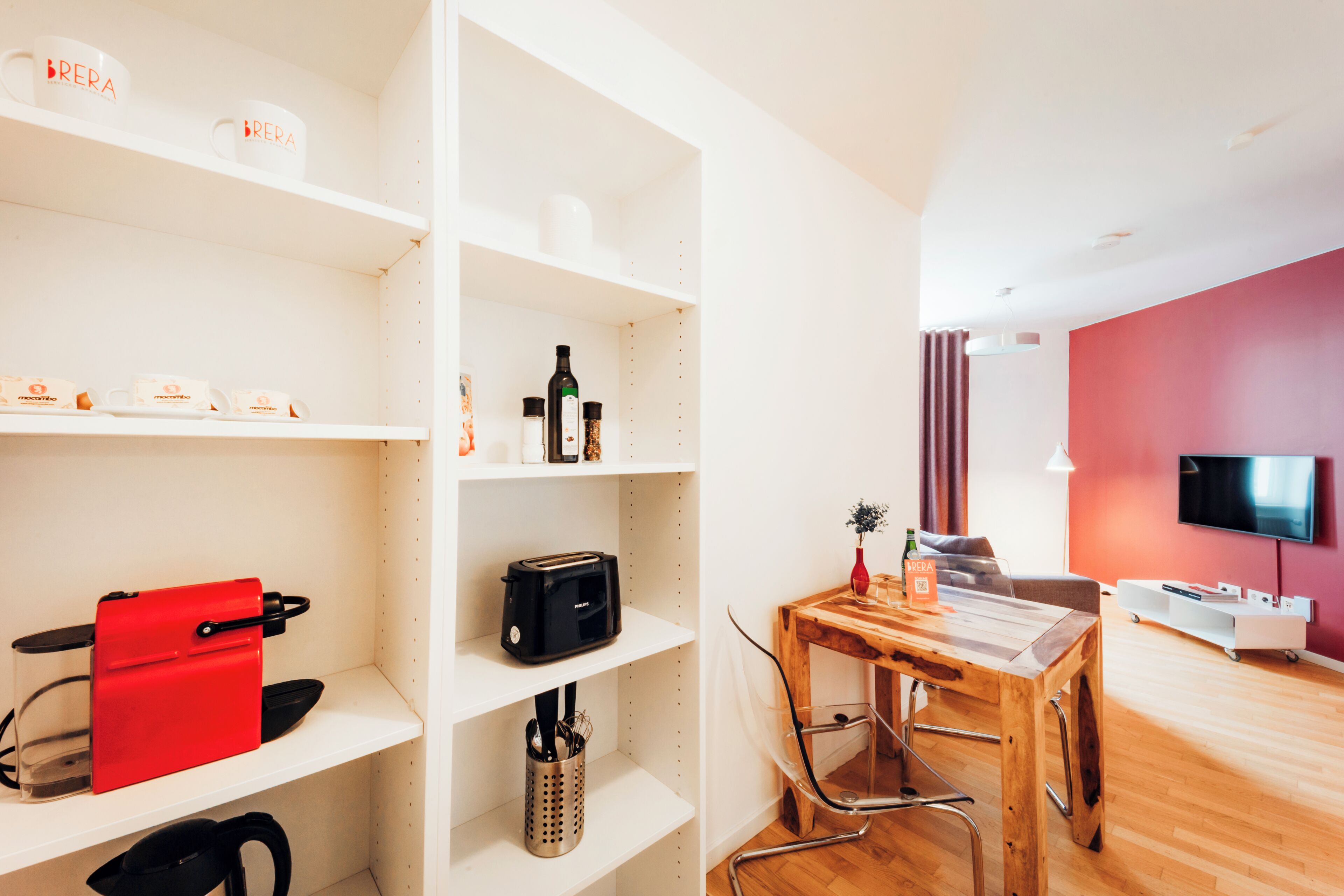 A modern living space with a dining area, a TV mounted on the wall, and a red sofa.