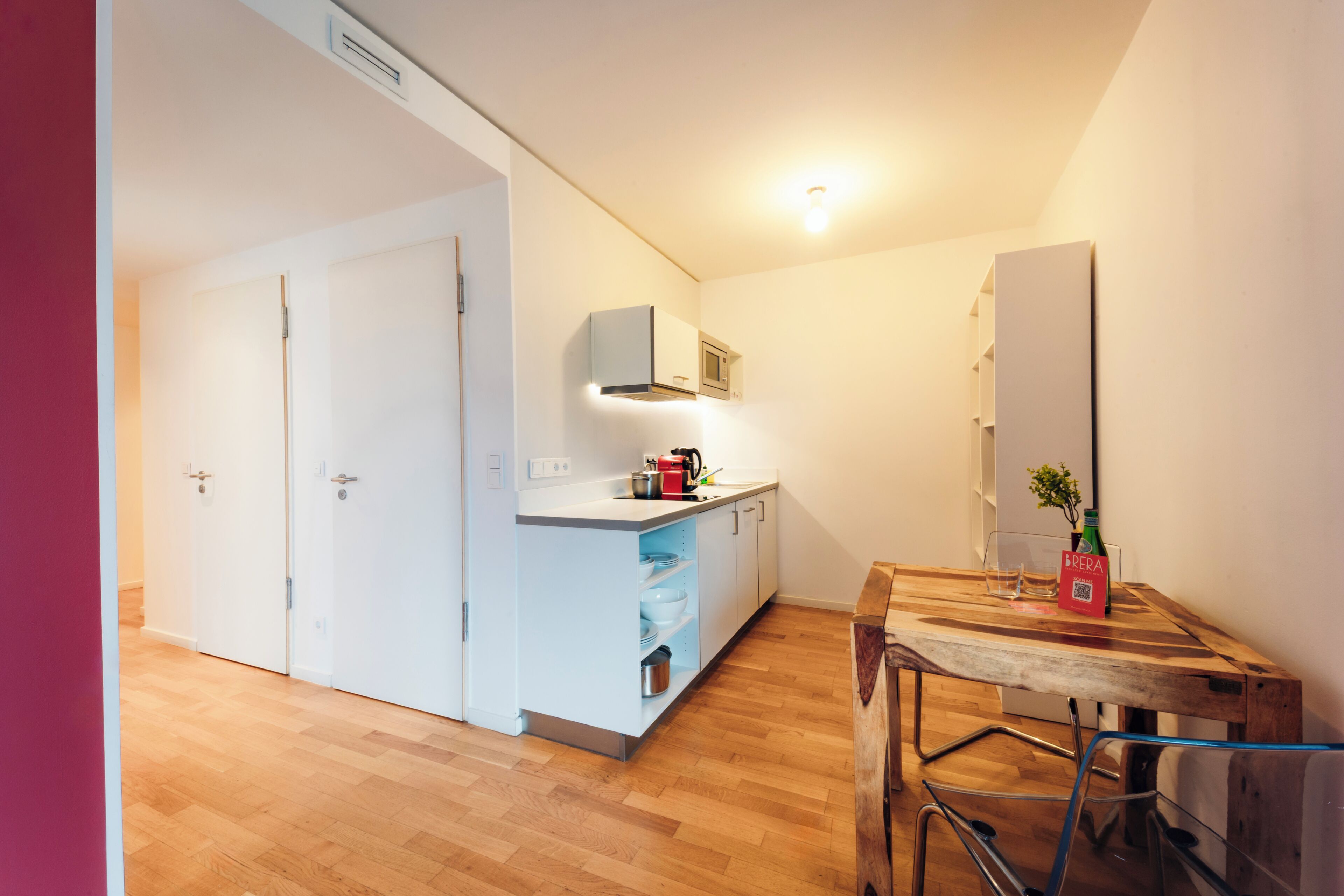 Una cocina compacta con armarios blancos, una mesa de comedor de madera y una pequeña encimera.