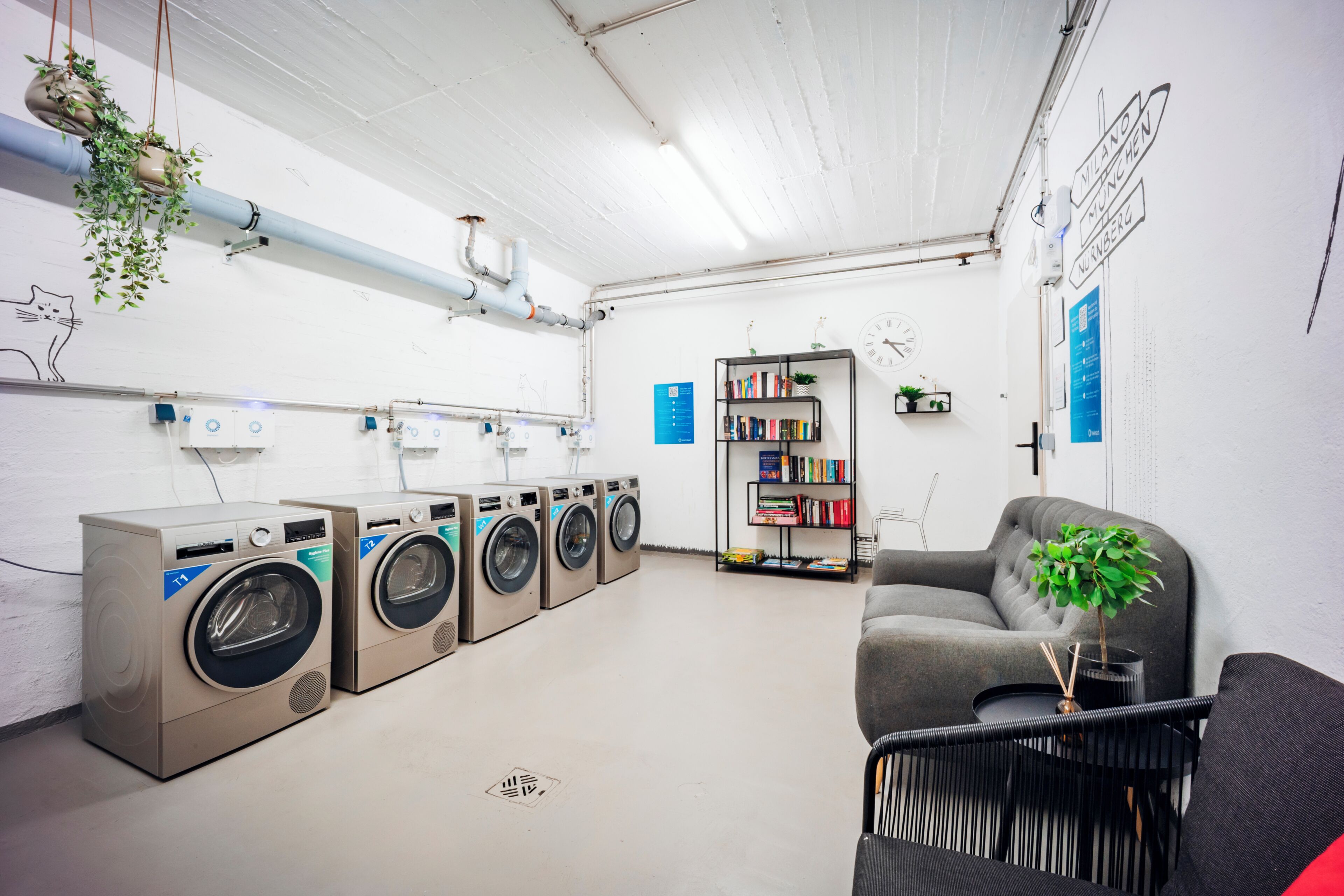 Un cuarto de lavandería con varias lavadoras, una estantería y una zona de estar.