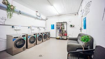Un cuarto de lavandería con varias lavadoras, una estantería y una zona de estar.