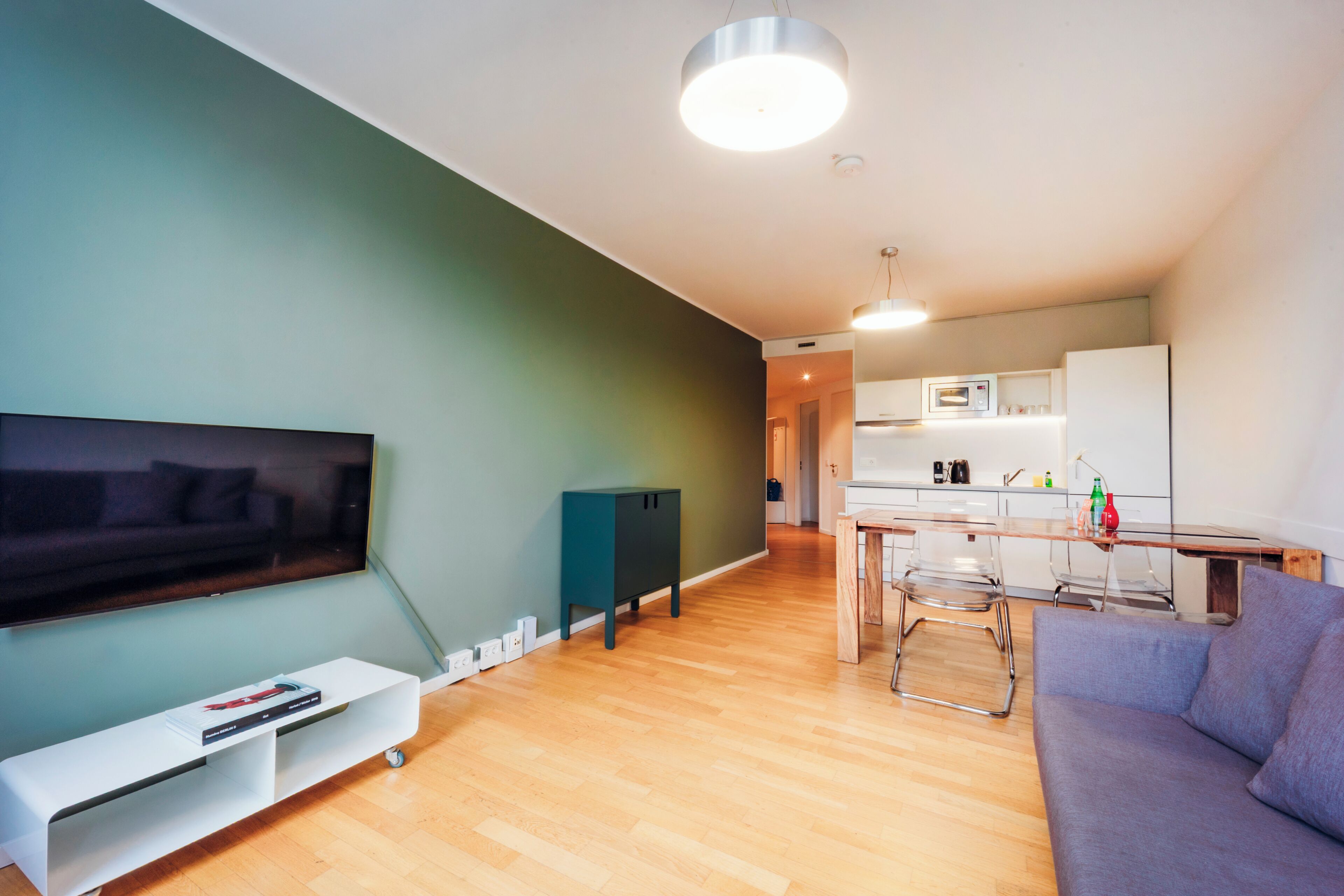 Ein modernes Wohnzimmer mit Fernseher, einer Couch und einem Essbereich inklusive Tisch und Stühlen.