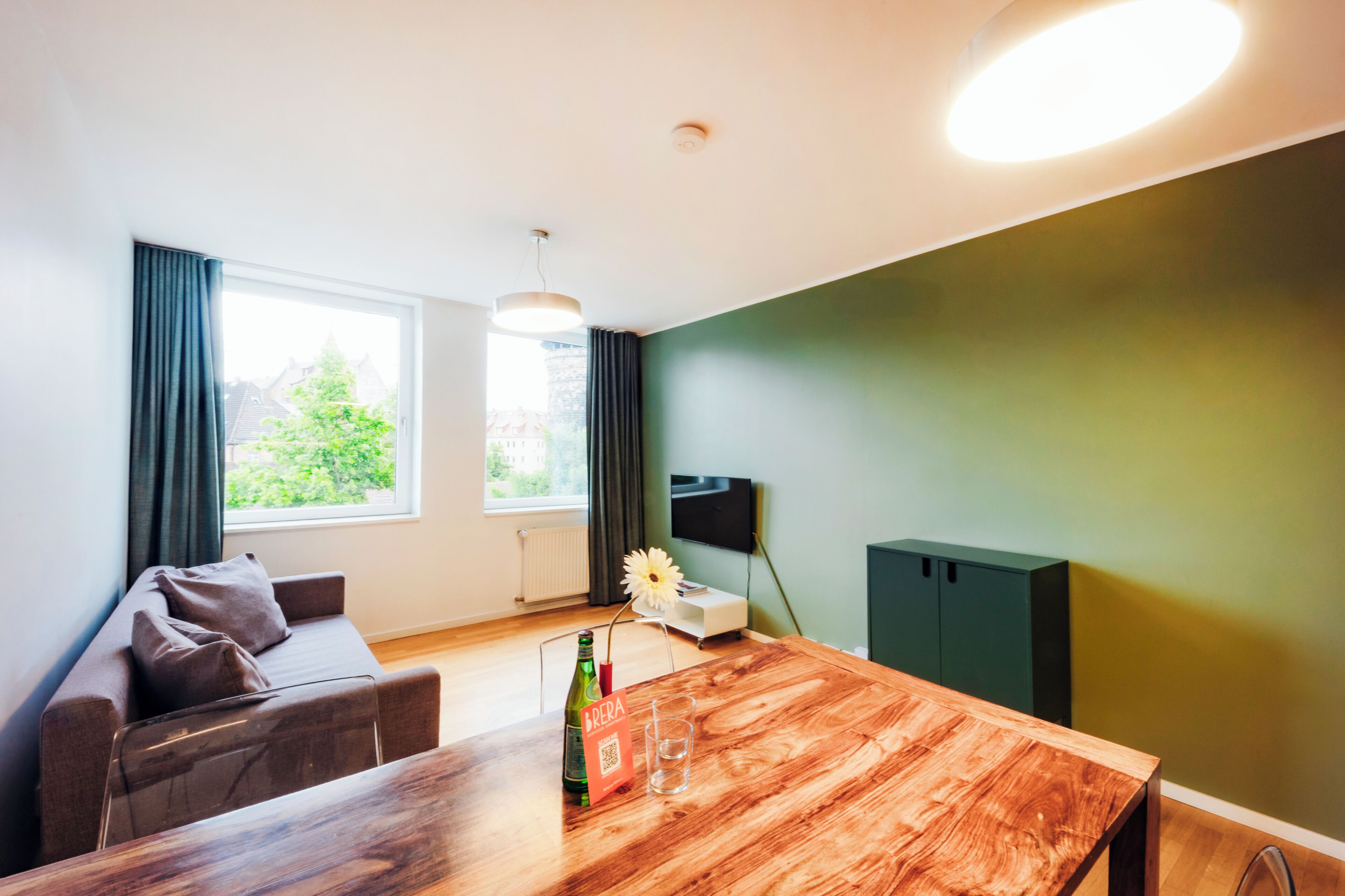 Una sala de estar moderna con una mesa de comedor de madera, un sofá, un televisor y una ventana con cortinas.