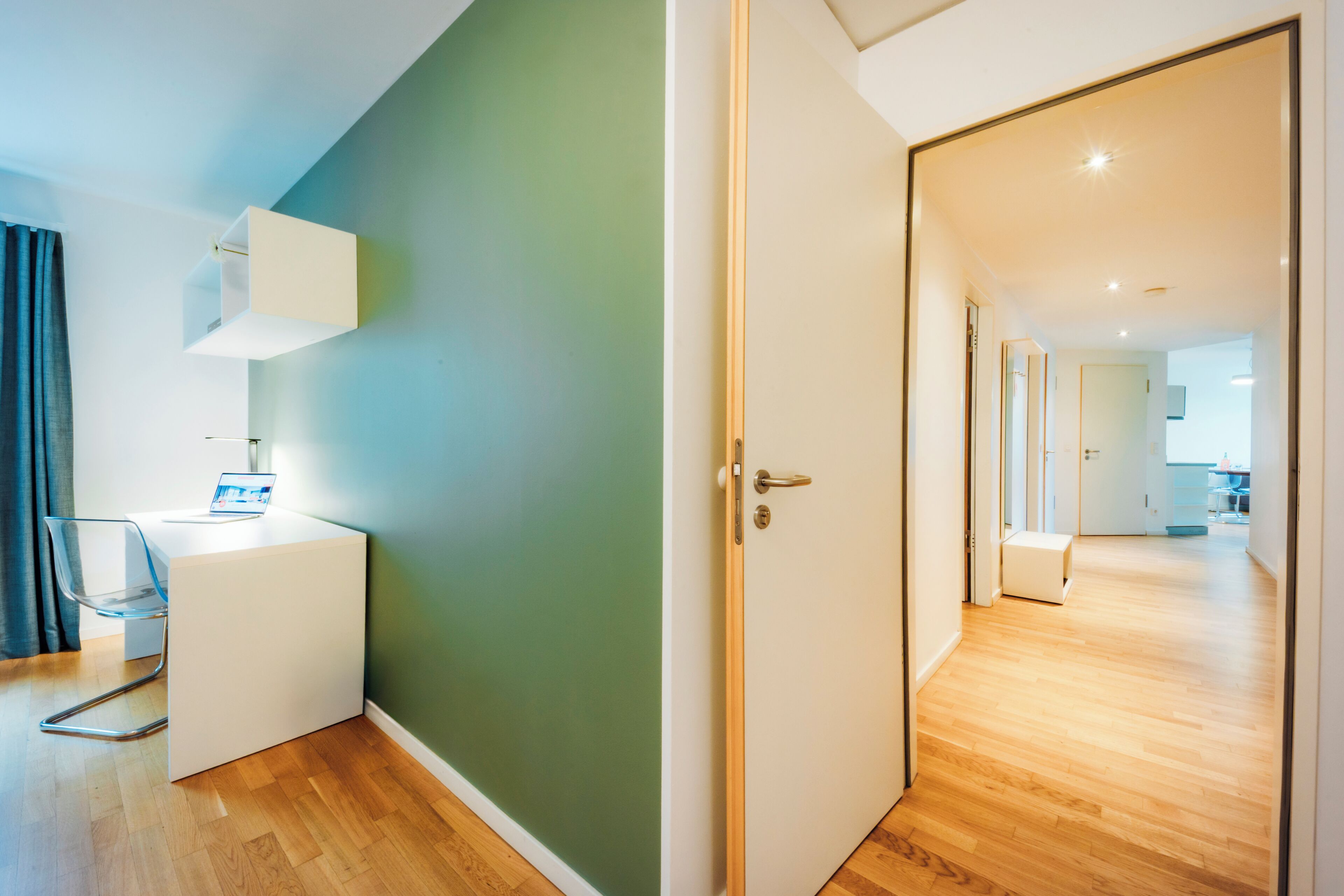 A modern room with a desk, chair, and a door leading to another area.