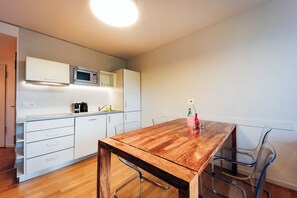 A modern kitchen with white cabinets, a microwave, and a wooden dining table with chairs. - Brera Serviced Apartments Nürnberg (Nuremberg)