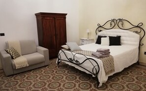 A bedroom with a bed, a sofa, a wardrobe, and a bedside table. - Agorà Suites & Apartments (Manduria)