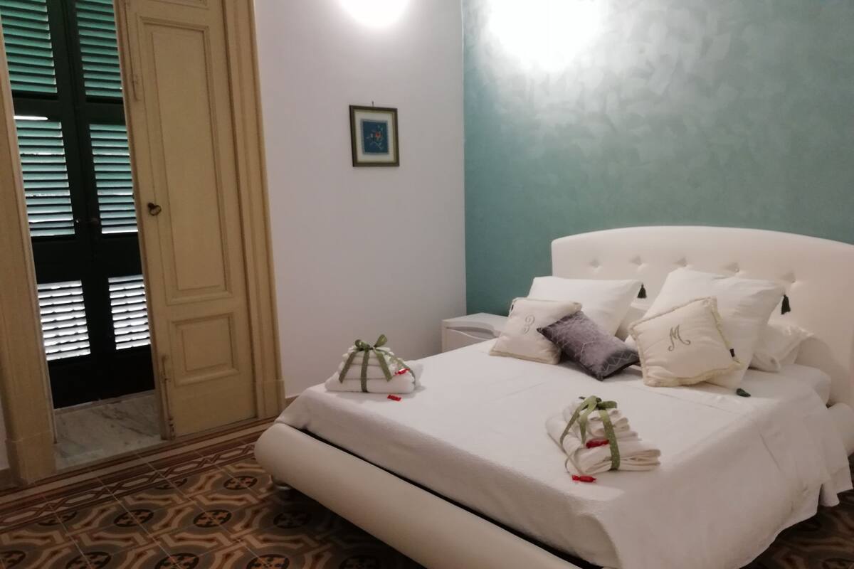 Ein Schlafzimmer mit Bett, Kissen, Nachttisch, einer Tür und einem Wandbild.