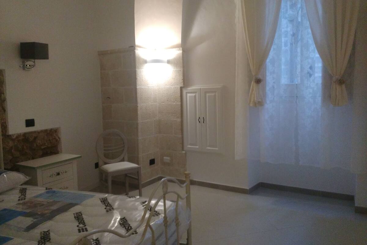 Ein Schlafzimmer mit Bett, Nachttisch, Stuhl, Kleiderschrank und einem Fenster mit Vorhängen.