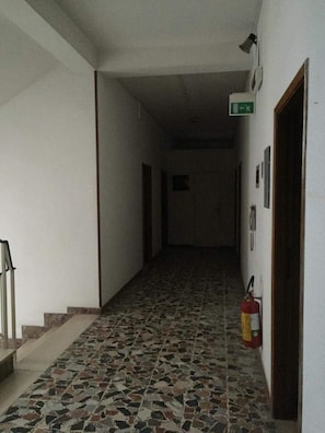 A hallway with a tiled floor, a fire extinguisher, and a door at the end.